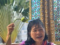 Kathy demonstrating how one dips a lotus into the holy water and then sprinkles it on one's head, while showing us a photo of the emerald Buddha in his three seasonal costumes.